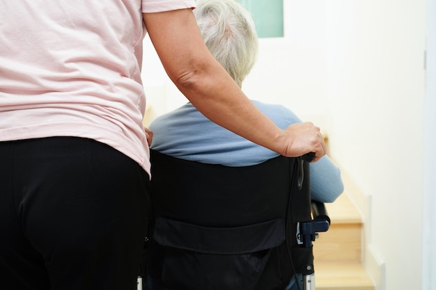 Asiatische ältere Frau im Rollstuhl mit Betreuungshilfe, die die Treppe hinunter geht, verhindert