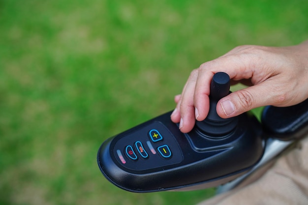 Asiatische ältere Frau mit Behinderung, die auf einem elektrischen Rollstuhl im medizinischen Konzept des Parks sitzt