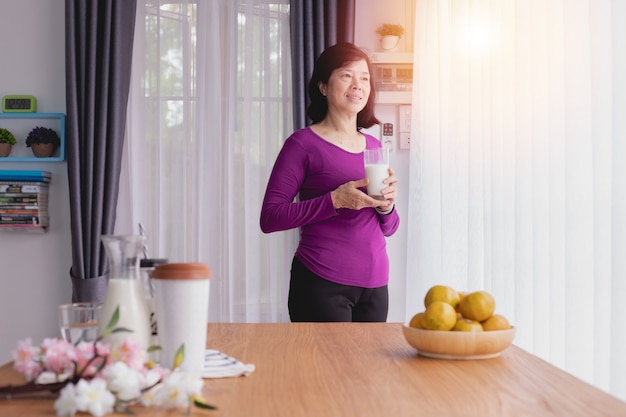 Asiatische ältere Leute etwas Milch trinken und Fenster heraus schauen.