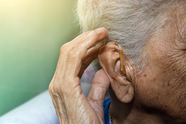 Asiatische ältere oder ältere Frau, die ein Hörgerät trägt, Nahaufnahme der Hand älterer Frauen, die ein Hörgerät tragen