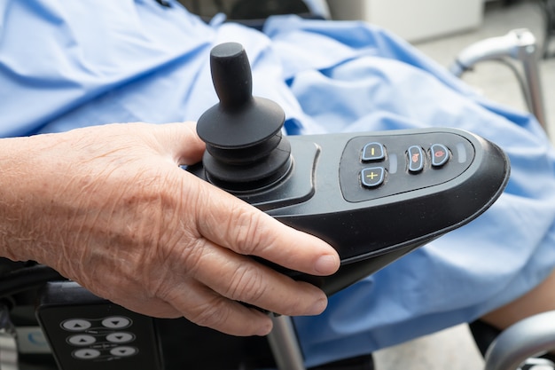 Foto asiatische ältere patientin auf elektrischem rollstuhl mit fernbedienung.