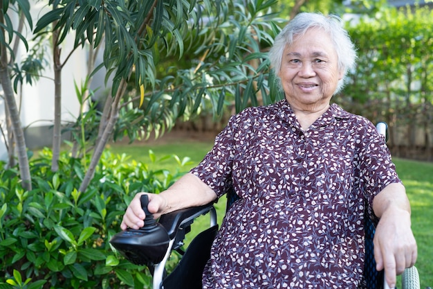 Asiatische ältere Patientin auf Elektrorollstuhl mit Fernbedienung