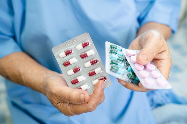 Asiatische ältere Patientin, die Antibiotika-Kapselpillen in Blisterverpackung hält