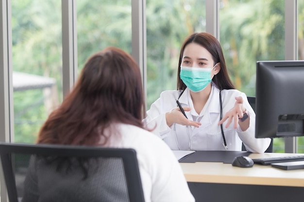 Asiatische ältere Patientin wird vom Arzt auf ihre Gesundheit überprüft, während beide eine medizinische Gesichtsmaske tragen