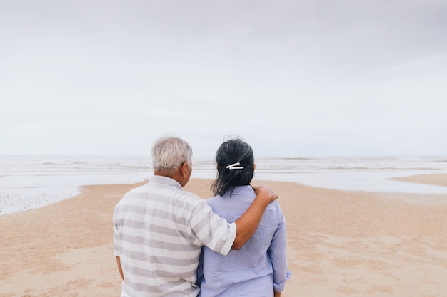 Asiatische alte ältere Paare, die am Strand am Meer gehen