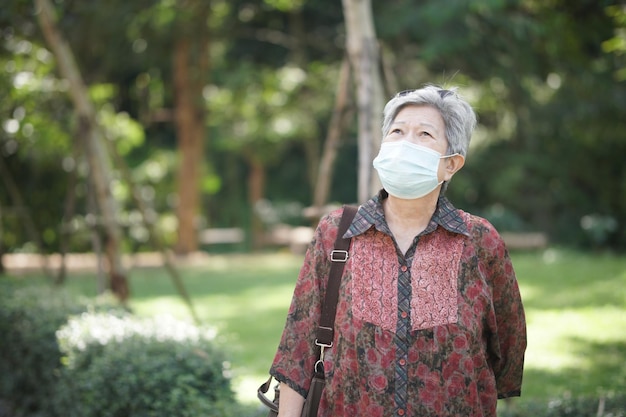 Asiatische alte ältere Seniorin mit Maske, die sich im Garten entspannt