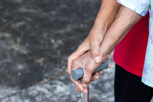 Asiatische alte Frau, die mit ihrer Hand auf einem Gehstock mit der Hand der Tochter steht