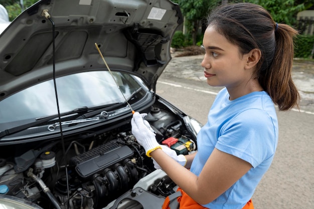 Asiatische Autotechnikerin in Uniform, die das Öl im Automotor überprüft