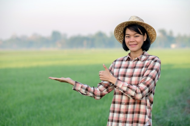 Asiatische Bäuerin lächelt und posiert mit dem Daumen nach oben auf einer grünen Reisfarm