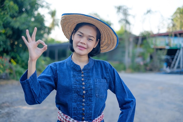 Asiatische Bäuerin trägt blaue Tracht Pose okay Hand auf dem Bauernhof