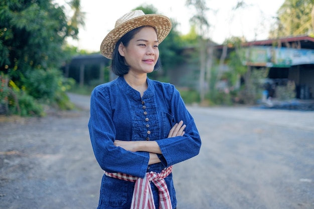 Asiatische Bäuerin trägt traditionelles Kostümlächeln und kreuzen die Hände auf dem Bauernhof