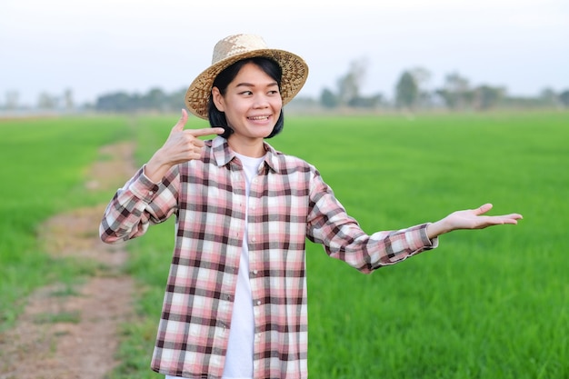 Asiatische Bauernfrau lächelt und schaut Pose heben Dinge an einer grünen Reisfarm