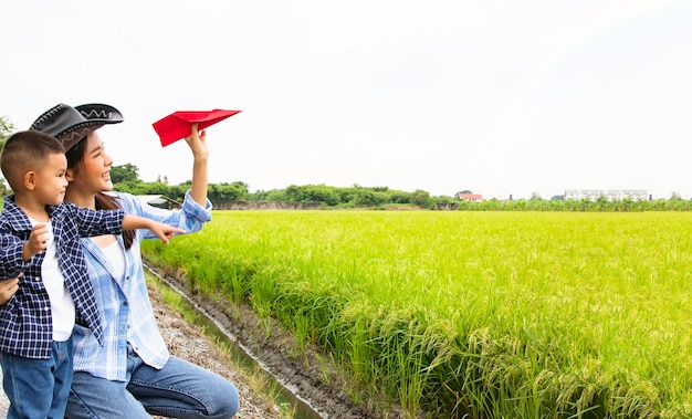 Asiatische Bauernmutter und Tochter spielen fröhlich fröhlich rote Papierflugzeuge auf grünen Reisfeldern.