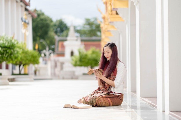 Asiatische buddhistische Frau in traditioneller Kleidung Thailands, die das alte Tripitaka-Buch Sanskrit von Lord Buddha Dhamma und Dharma-Buch Sanctuary Ratchanatdaram Bangkok liest