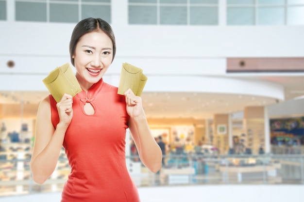 Asiatische Chinesin in einem cheongsam Kleid, das rote Umschläge hält