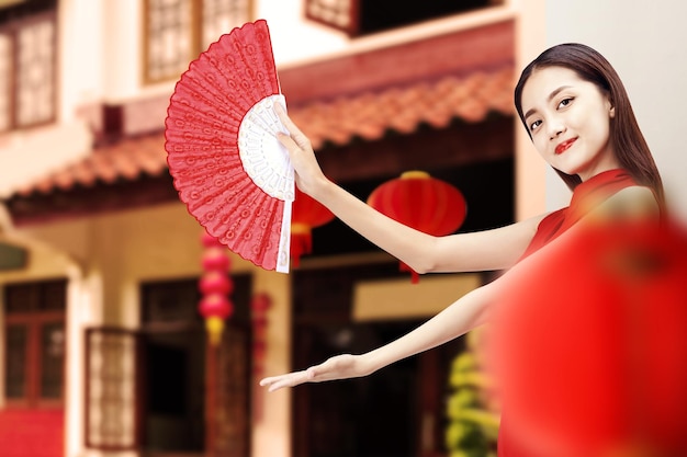 Asiatische Chinesin in einem Cheongsam-Kleid mit Fächer und offener Handfläche, die etwas zeigt. Frohes chinesisches Neujahr