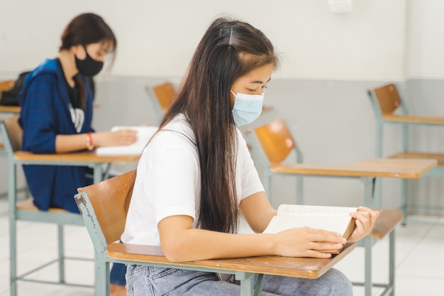 Asiatische College-Studenten, die zurück in die Schule gehen, tragen Gesichtsmasken und halten Abstand zum Lernen im Klassenzimmer