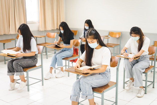 Asiatische College-Studenten kehren mit Gesichtsmaske zur Schule zurück und halten soziale Distanz, während sie im Klassenzimmer lernen, um eine COVID-19-Pandemie zu verhindern