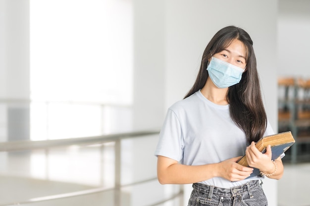 Asiatische College-Studentin in entspannter Freizeit zurück zur Schule mit medizinischer Gesichtsmaske auf dem Campus