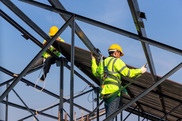 Asiatische Dachbauer tragen Sicherheitshöhenausrüstung, um den Dachrahmen zu installieren. Absturzsicherungsvorrichtung für Arbeiter mit Haken für Sicherheitsgurte auf der Baustelle.