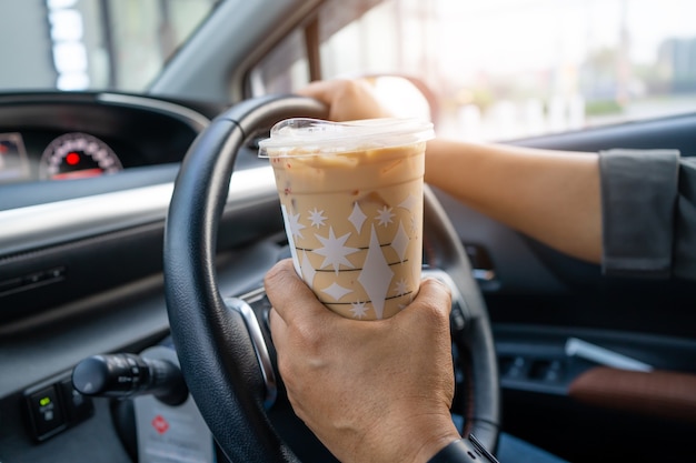 Asiatische Dame, die Eiskaffee für Getränkessen im Auto hält.