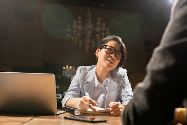 Asiatische Dame, die mit Kollegin im dunklen Büro arbeitet