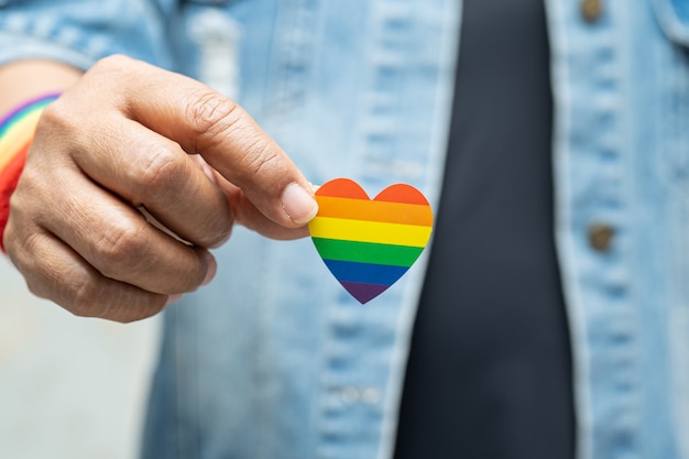 Asiatische Dame, die Regenbogenfarbflaggenherzensymbol des LGBT-Stolzmonats hält