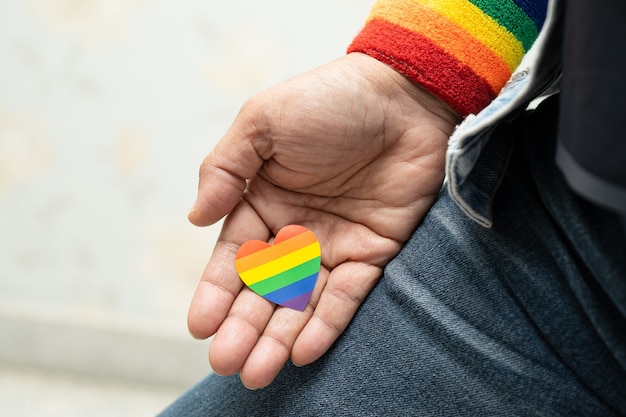 Asiatische Dame, die Regenbogenfarbflaggenherzensymbol des LGBT-Stolzmonats hält