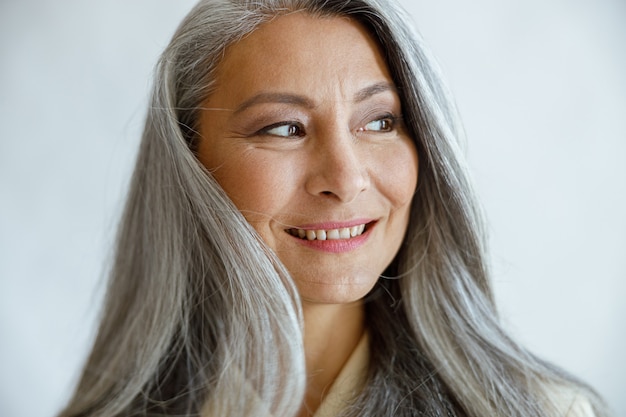 Asiatische Dame mit losen grauen Haaren posiert für die Kamera auf hellem Hintergrund