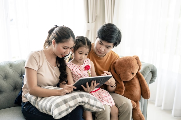 Asiatische Eltern und ein Kind schauen sich zu Hause einen Laptop an. Familienkonzept.