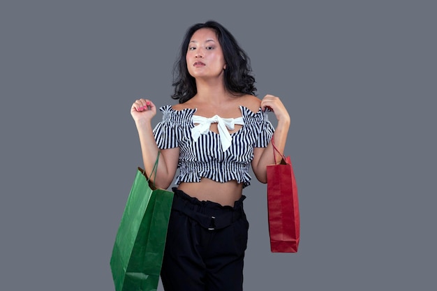 Asiatische ethnische Frau mit Einkaufstüten isoliert auf grauem Hintergrund