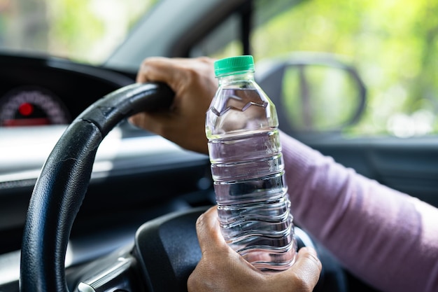 Asiatische Fahrerin, die eine Flasche für Trinkwasser hält, während sie ein Auto fährt Wärmflasche aus Kunststoff verursacht Feuer