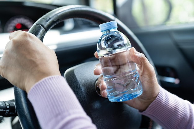 Asiatische Fahrerin, die eine Flasche für Trinkwasser hält, während sie ein Auto fährt Wärmflasche aus Kunststoff verursacht Feuer