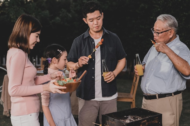 Asiatische Familie, die zu Hause eine Grillparty hat. Gegrillter Grill zum Abendessen im Hinterhof kochen. Lebensstil im Sommerurlaub.