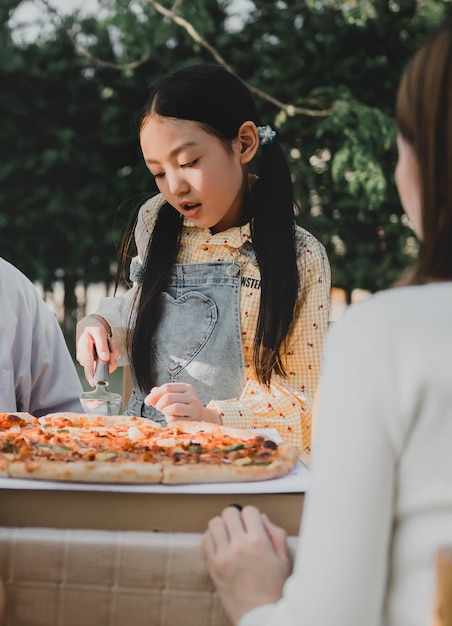 Asiatische Familie, die zu Hause Pizza im Garten isst. Eltern mit Kind und Großvater leben im Hinterhof.