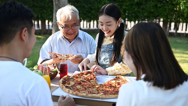 Asiatische Familie, die zu Hause Pizza im Garten isst. Elternteil mit Kind und Großvater Lebensstil im Hinterhof.