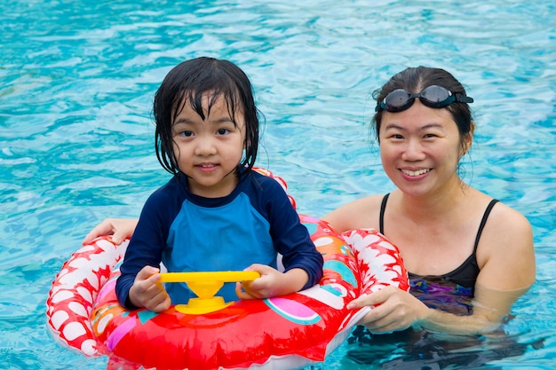 Asiatische Familie im Schwimmenrohr, das auf Swimmingpool spielt