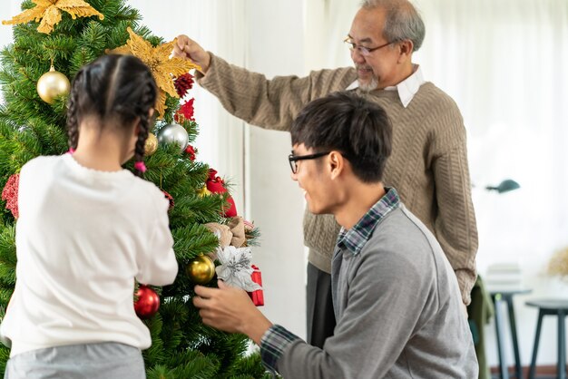 Asiatische Familie mit mehreren Generationen, die einen Weihnachtsbaum schmückt.