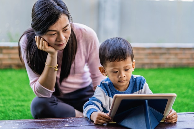 Asiatische Familie mit Sohn schauen die Karikatur über Technologietablette und spielen zusammen
