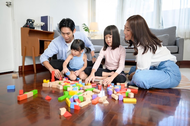 Asiatische Familie mit spielenden und bauenden Kindern aus bunten Holzspielzeugblöcken im Wohnzimmer