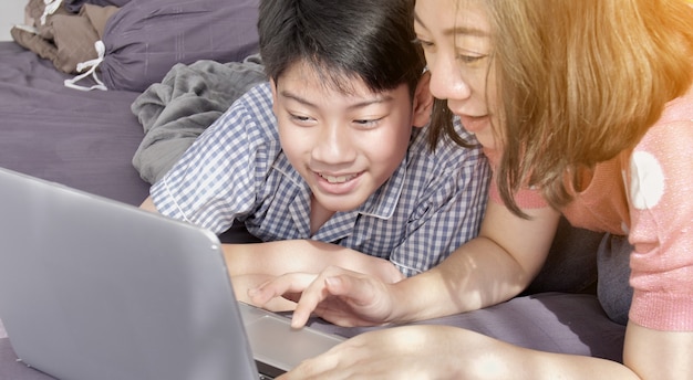 Asiatische Familienmutter und -sohn, die auf Laptop-Computer aufpasst.