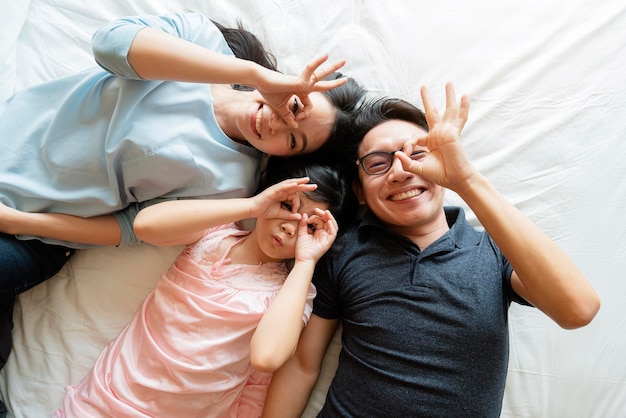 Asiatische Familienmutter, Vater und Tochter, die ein lustiges Schlafspiel im Hintergrund des Wohnzimmers machen