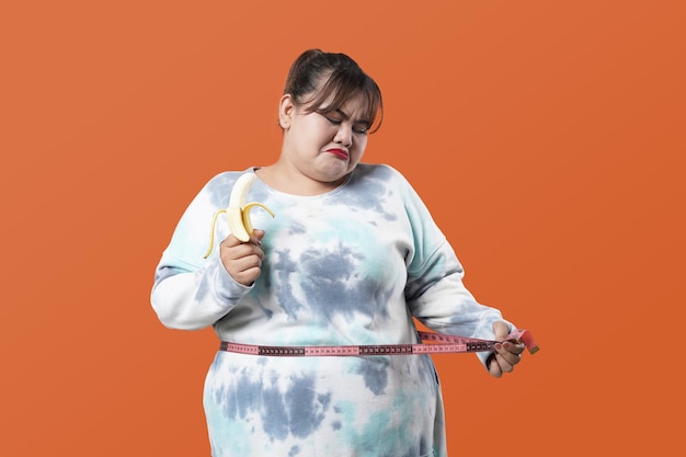 Asiatische fettleibige Frau mit dickem Bauch, die Fettfalten auf dem Bauch hält. Konzept von Übergewichtsproblemen