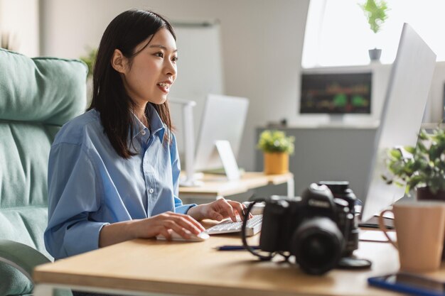 Asiatische Fotografin, die am Computer arbeitet und Fotos im Innenbereich bearbeitet