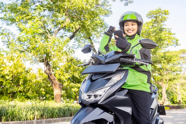 Asiatische Frau arbeitet als Motorradtaxifahrerin und überprüft die Bestellung auf ihrem Handy