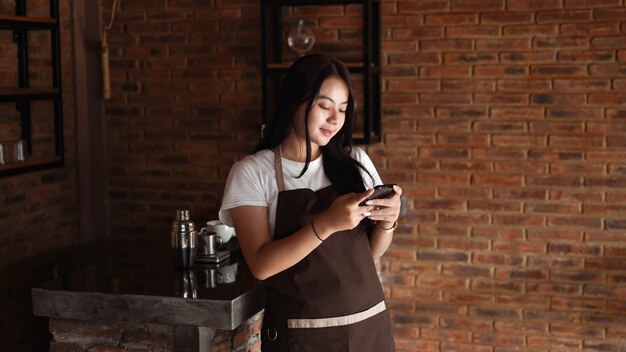 Asiatische Frau Barista lächelt und hält Telefon. Überprüfen Sie die Online-Bestellung beim Kunden.