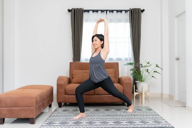 Asiatische Frau beim Yoga und Stretching im Wohnzimmer zu Hause Das Konzept der Übung, um einen gesunden Körper für sich selbst zu schaffen