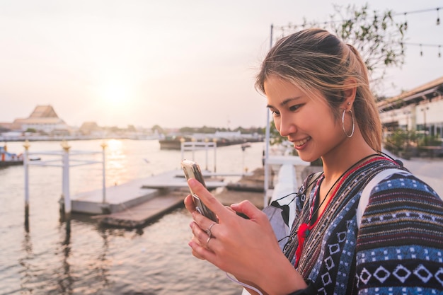 Asiatische Frau benutzt Handy, während sie bei Sonnenuntergang im Fluss Chao Phraya in Bangkok unterwegs ist