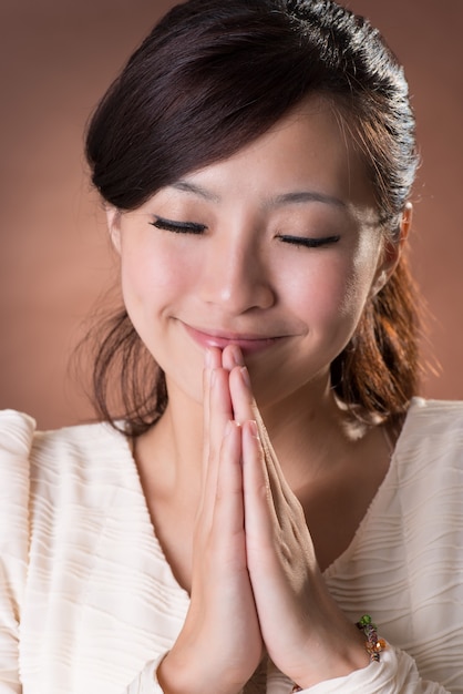 Asiatische Frau betend, Nahaufnahmeporträt auf Studio braunem Hintergrund.