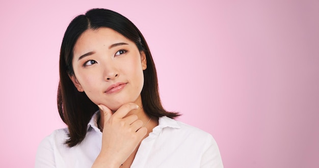 Asiatische Frau denkt und entscheidet über Mockup-Raum bei der Problemlösung vor einem rosafarbenen Studiohintergrund. Weibliche Person mit Ideenlösung oder Wahlmöglichkeit in Erinnerungserinnerung oder Brainstorming auf Mock-up